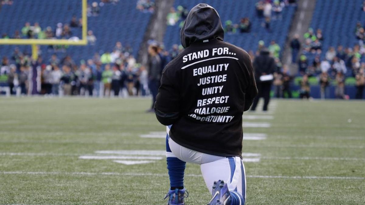 An Indianapolis Colt player kneels on the field Sunday during warmups before an NFL football game against the Seattle Seahawks in Seattle. The unidentified player is wearing a special team T-shirt in reference to recent protests during the singing of the national anthem at NFL football games. (AP Photo/Elaine Thompson)