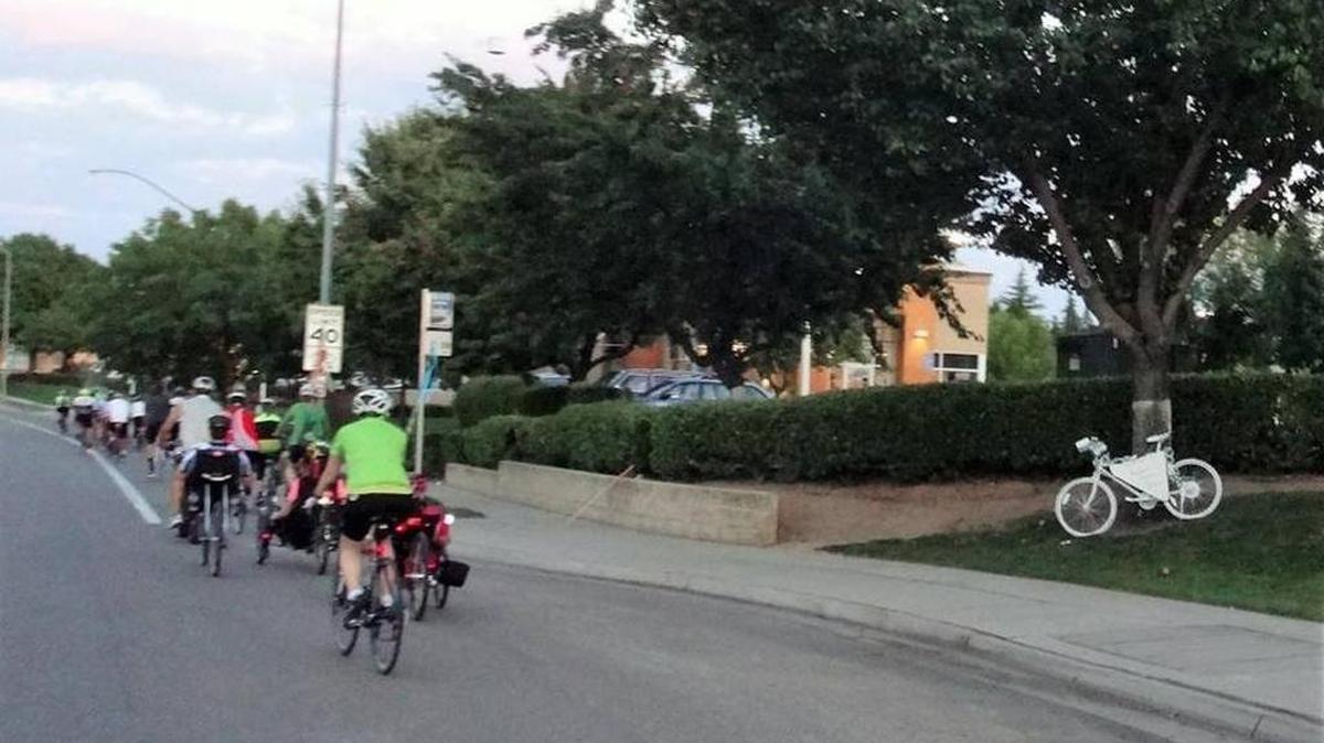A white “ghost” bike, right, honors a Fresno-area cyclist who was killed while riding. At left, cyclists participate in the annual Ride of Silence on May 18.