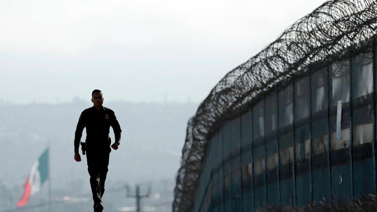 Border Patrol agent Eduardo Olmos walks near the secondary fence separating Tijuana, Mexico, background, and San Diego in San Diego. On Tuesday, Trump threatened to use the military on the U.S.-Mexico border until his promised wall is built.