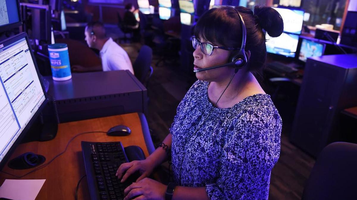 Cast in a blue light of an otherwise darkened room, Lydia Valdez, an ESD II, handles a call at the Fresno Police Department’s Dispatch Center Monday, July 30, 2018 in Fresno.