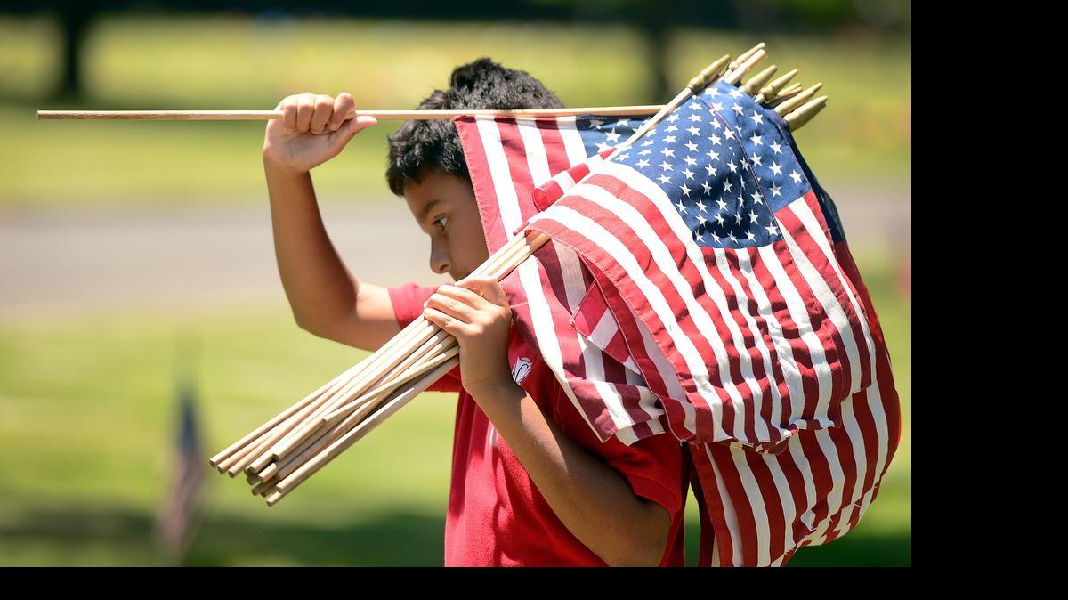 
Alex Grewal carries a bundle of American Flags as he helps place them on the headstones of a military veterans at Fresno’s Belmont Memorial Park in preparation for Memorial Day last year. There are an estimated 10,000 military veterans buried at Belmont Memorial. 
