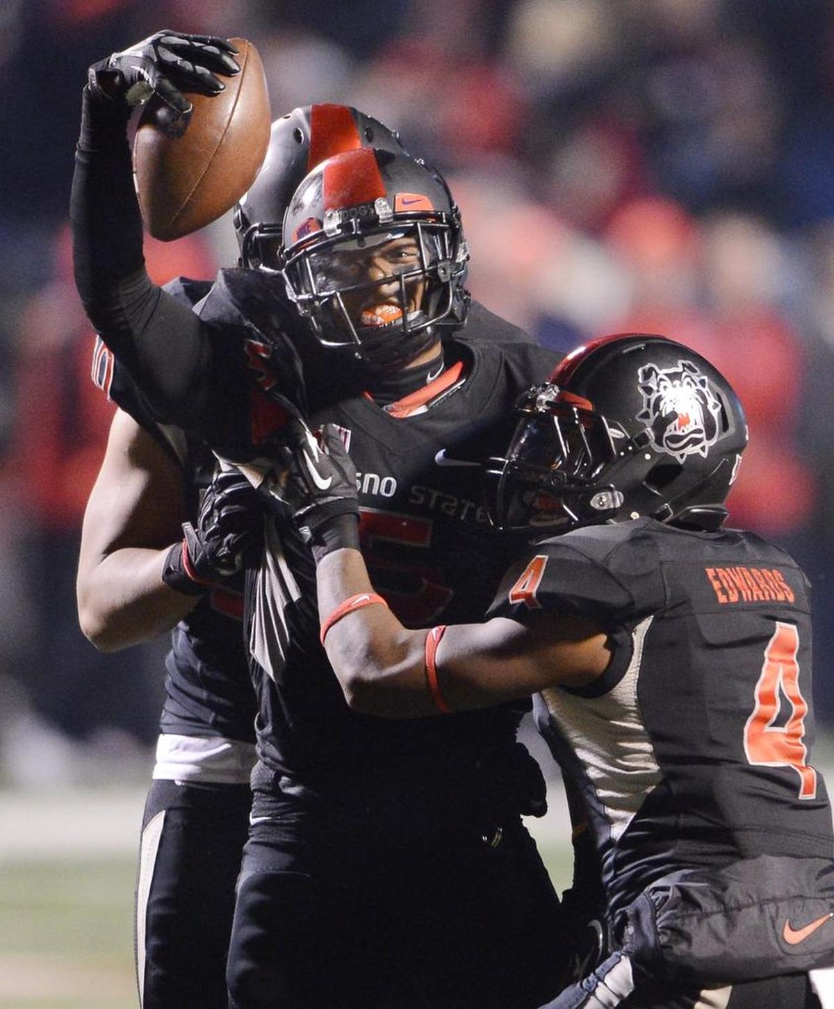 Fresno State safety Dalen Jones, center, holds up the ball as he celebrates with Shannon Edwards after Jones intercepted a pass to secure the Bulldogs’ win against Utah State in the Mountain West Conference championship game at Bulldog Stadium in December 2013.
