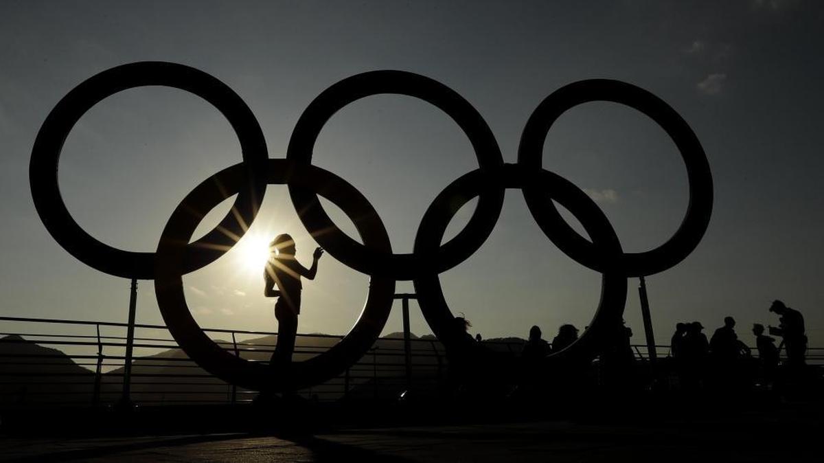 A woman is silhouetted by the setting sun as she looks at a set of Olympic rings in the Olympic Park in Rio de Janeiro on Thursday, Aug. 4, 2016.