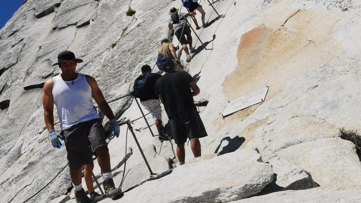 A group of hikers use the cables to acsend the final 400 feet to the top of Half Dome. Below people pick from a pile of gloves left by other hikers to aid in climbing steel cables that heat up in the sun.
