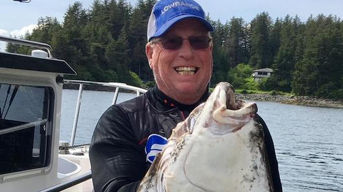 Roger George grimaces to hold up his 62-inch, 130-pound-plus halibut caught on his Alaskan fishing trip.