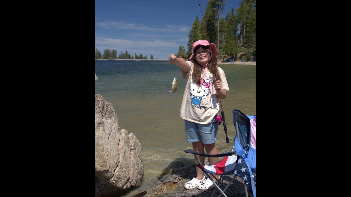 A young angler is all smiles after hooking a fish during the annual Greg Mark’s Shaver Lake Youth Fishing Derby .