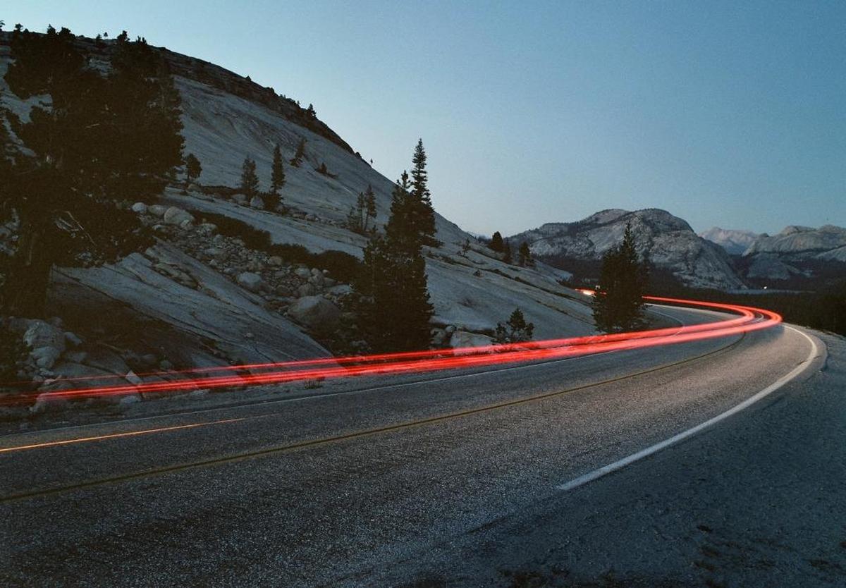 In this mid-September 2005 scene, traffic passes Olmstead Point at dusk, moving eastward along the Tioga Pass Road toward Tenaya Lake, seen at the far right.