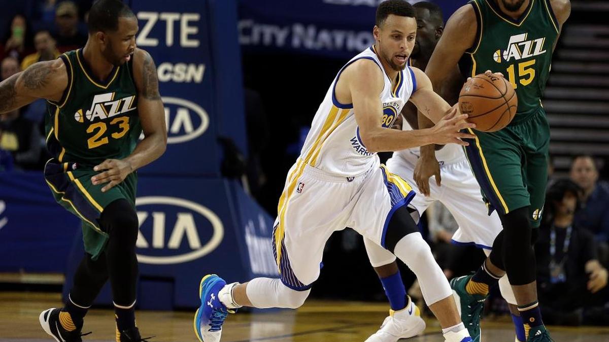 The Warriors Stephen Curry drives the ball between Utah Jazz defendes Chris Johnson (23) and Derrick Favors during the first half of Wednesday night’s game in Oakland.