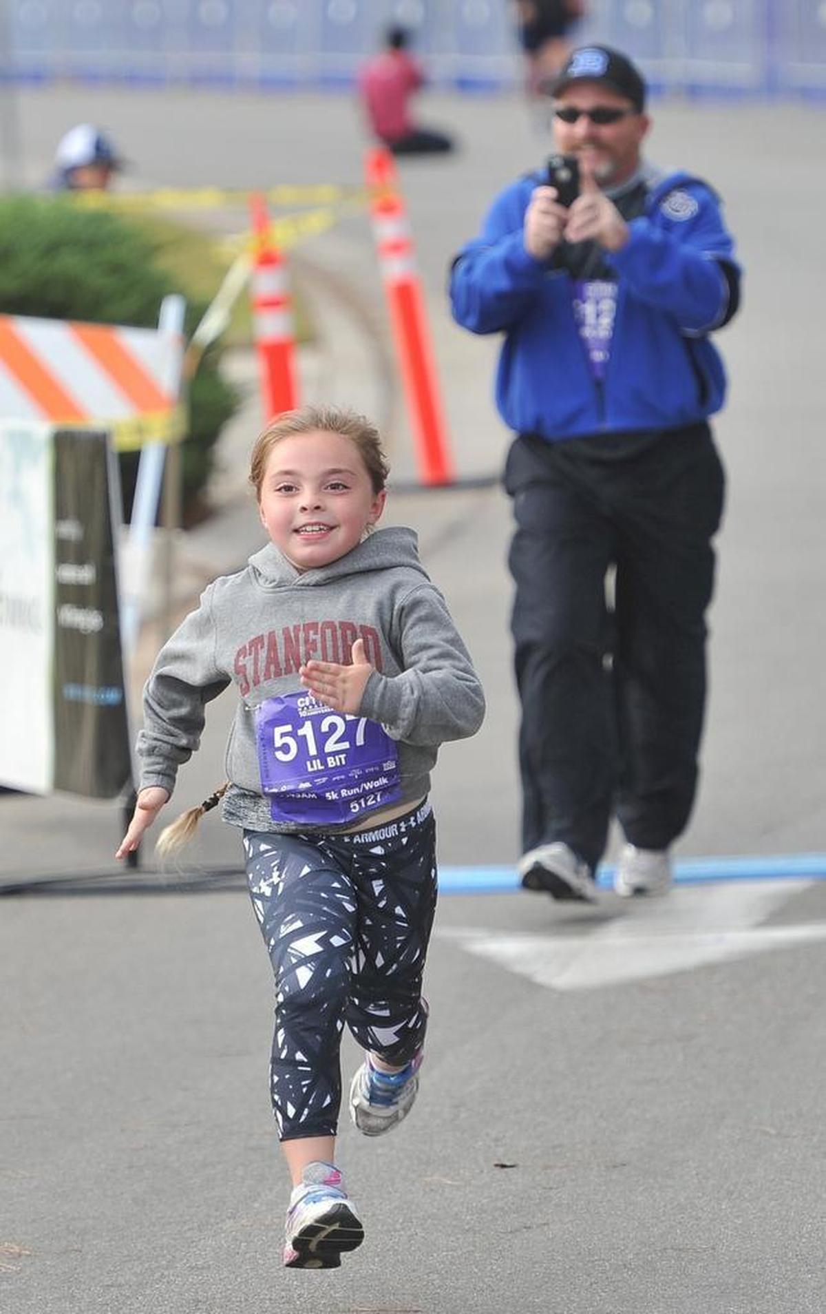 Samantha Roche, 7, makes a dash for the finish line in the 5K Run/Walk, as dad Darden Roche, background, documents her finish, during the Two Cities Marathon & Half Sunday morning, Nov. 5, 2017.