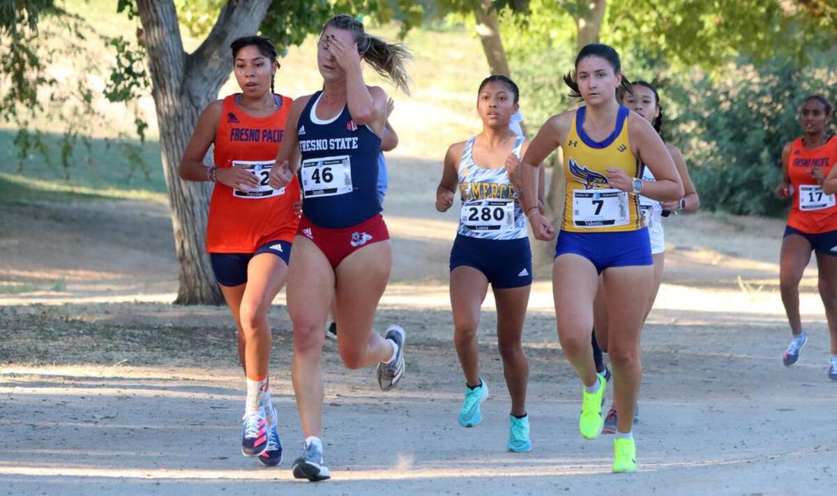 Fresno State sophomore Corie Smith wipes her forehead as the 5K race pack nears the mile mark during the Sept. 3, 2022 Seawolf Invitational at Woodward Park. Maribel Aguilar of Fresno Pacific and Helena Valentic of Cal State Bakersfield surround her.