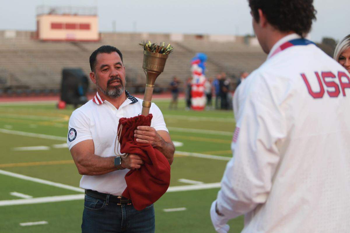 Richard Torrez Jr. about to take a torch handed to him by his father Richard Torrez Sr. to light the Olympic flame replica during the welcome home celebration at the Bob Mathias Stadium in Tulare on Aug. 21.