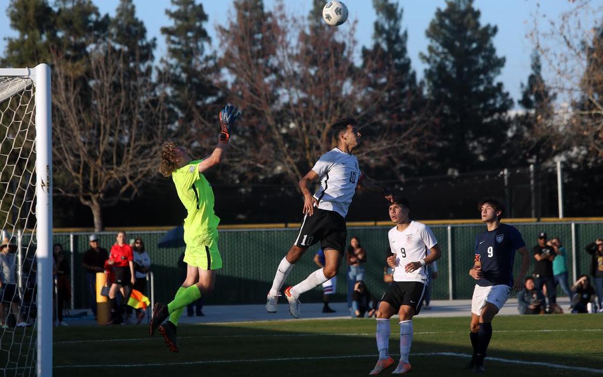 Clovis East goalie Kyle LaGrasse leaps to keep the ball away from Central High midfielder Alan Gutiérrez in the Feb. 11, 2022 showdown for the TRAC championship. Central won, 2-1, and both teams tied for the league title with 7-2-1 records.