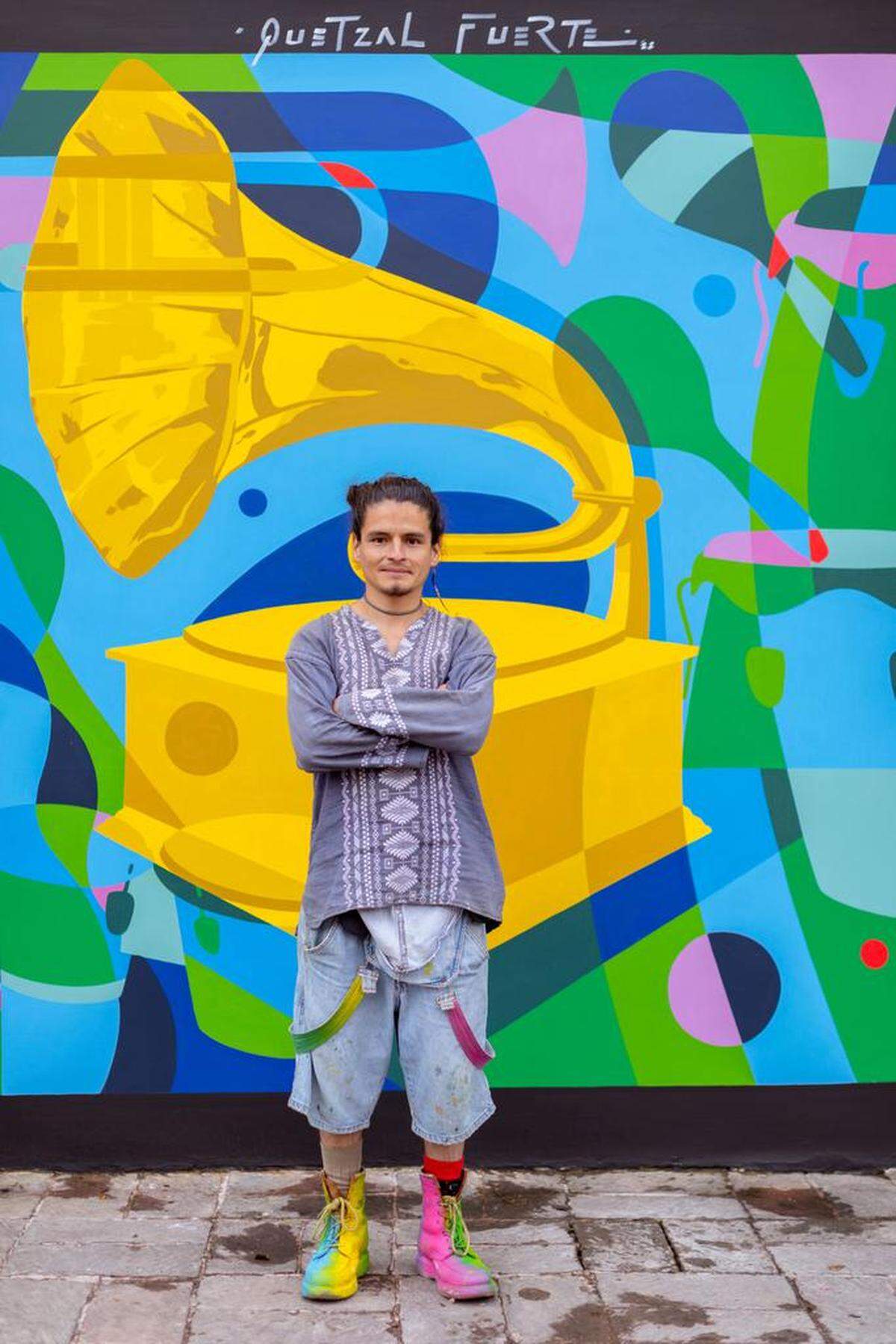 Fotografía cedida por la Academia Latina de la Grabación donde aparece el muralista mexicano Quetzal Fuerte mientras posa junto al mural con el gramófono, que es el símbolo de la Academia, y otros instrumentos musicales, pintado en Morelia.