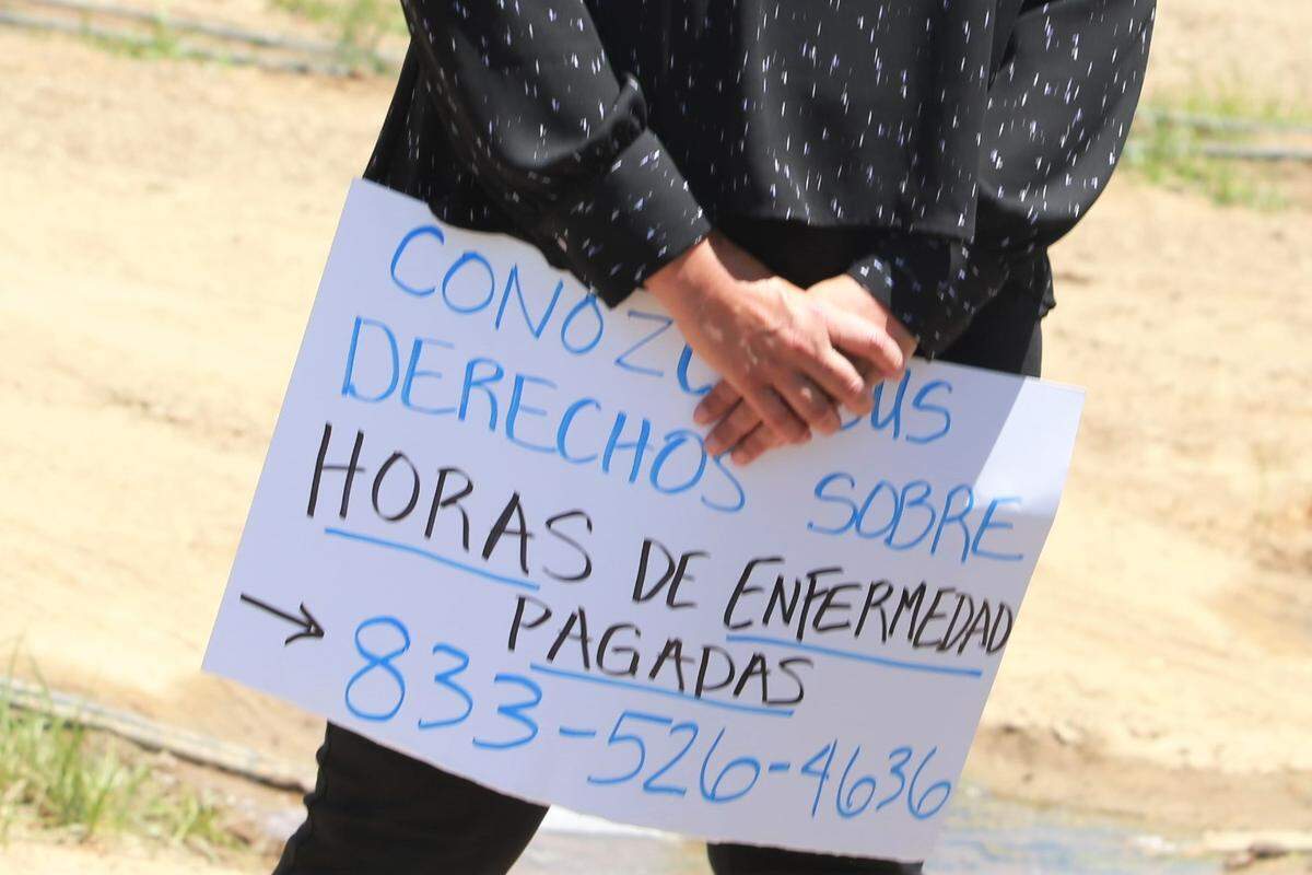 Labor Commissioner Lilia García-Brower holds a poster with the phone where farmworkers can call to know their rights at one of the fields in the Goshen area during the dissemination of information to workers in the fields during the caravan mobile in Tulare County in June 2021.