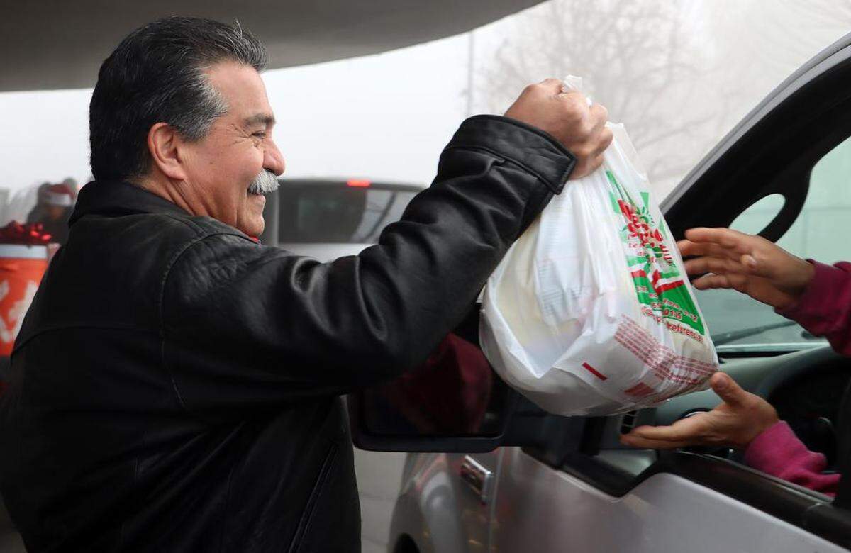 Dr. José Luis Bautista hands out a bag of food during the 25th annual Navidad en el Barrio at the Bautista Medical Group parking lot in downtown Fresno on Dec. 17, 2022.