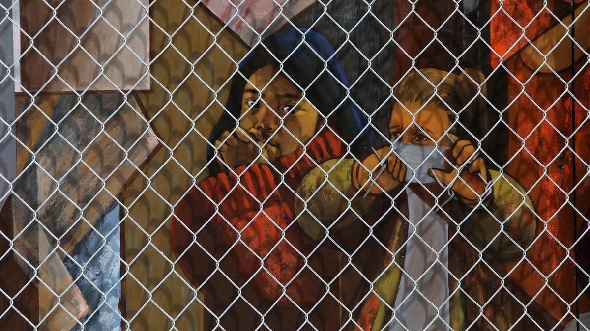 Two children peer out from behind a chain link fence in the 'Children in Cages' mural by Lalo García that was set up May 16, 2021 at the Fulton Mall.