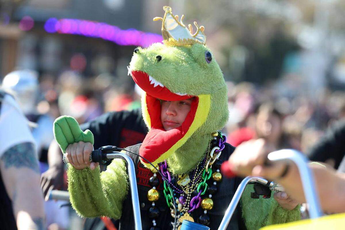 A “dinosaur” rides a bike along Olive Avenue during the 25th annual Mardi Gras Parade in the Tower District on Feb. 19, 2023.