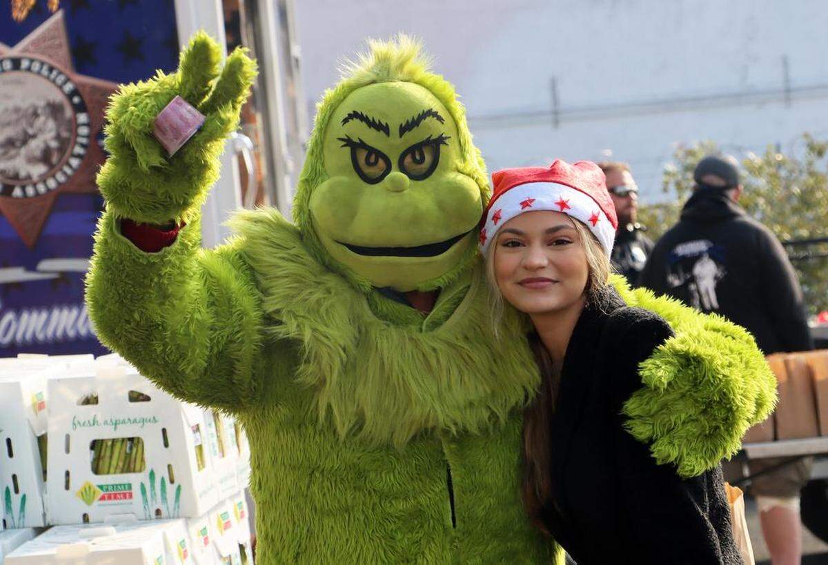 The Grinch greets a volunteer at the Christmas With Lulu toy and food giveaway in Chinatown on Dec. 17, 2022. The event was sponsored by the Lulu Foundation with support from the Fresno Police Officers Association.