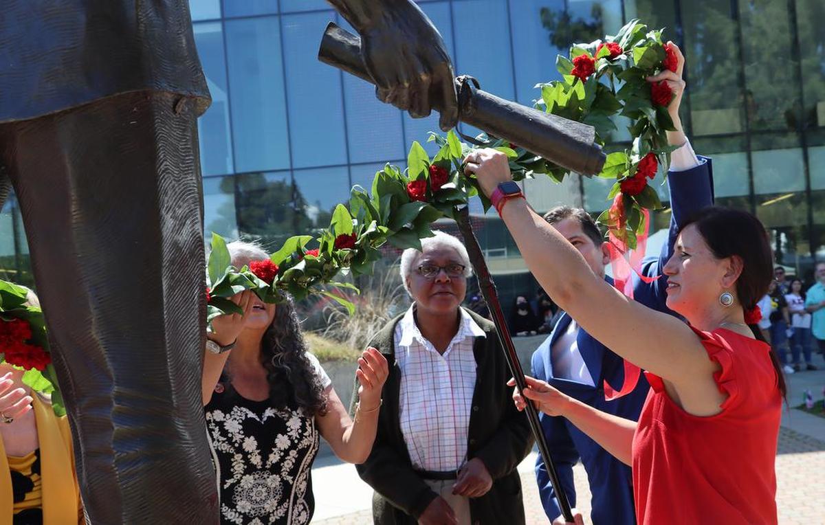 Ofelia Gámez helps place a garland around the bronze statue of farmworker leader César E. Chávez during a ceremony honoring him at Fresno State’s Peace Garden on March 24, 2022.