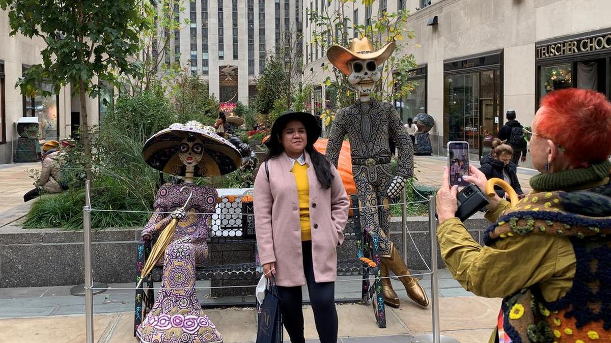 Una mujer posa frente a dos catrinas del Día de los Muertos instaladas hoy en una de las plazas del Rockefeller Center en Nueva York.