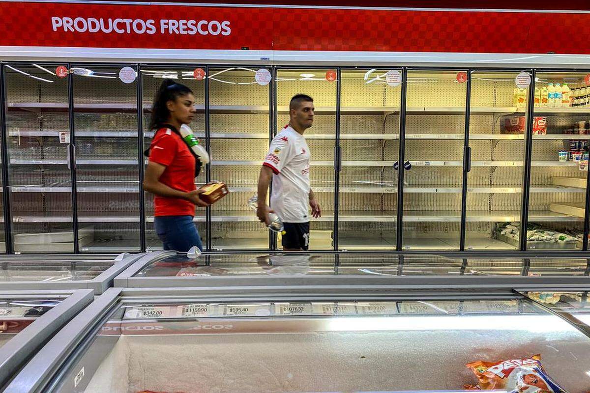 Dos personas caminan frente a las neveras casi vacías de un supermercado, hoy, en Buenos Aires.