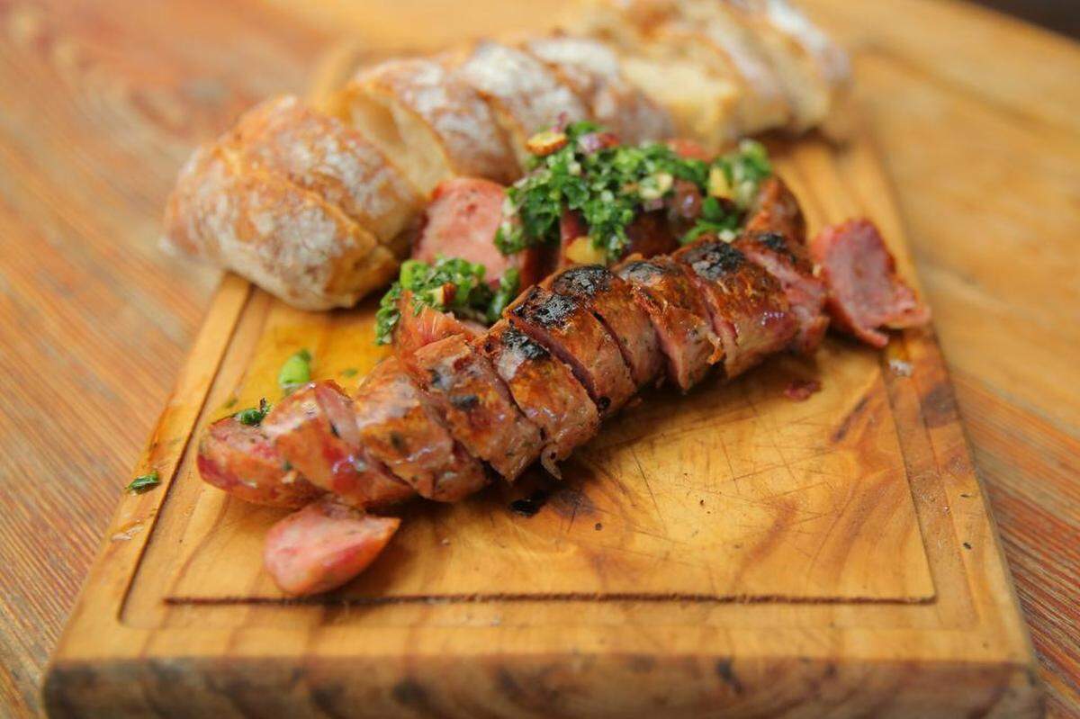 Fotografía de trozos de chorizo servidos en tabla durante un asado en la casa del asador profesional uruguayo Sebastián Manito.