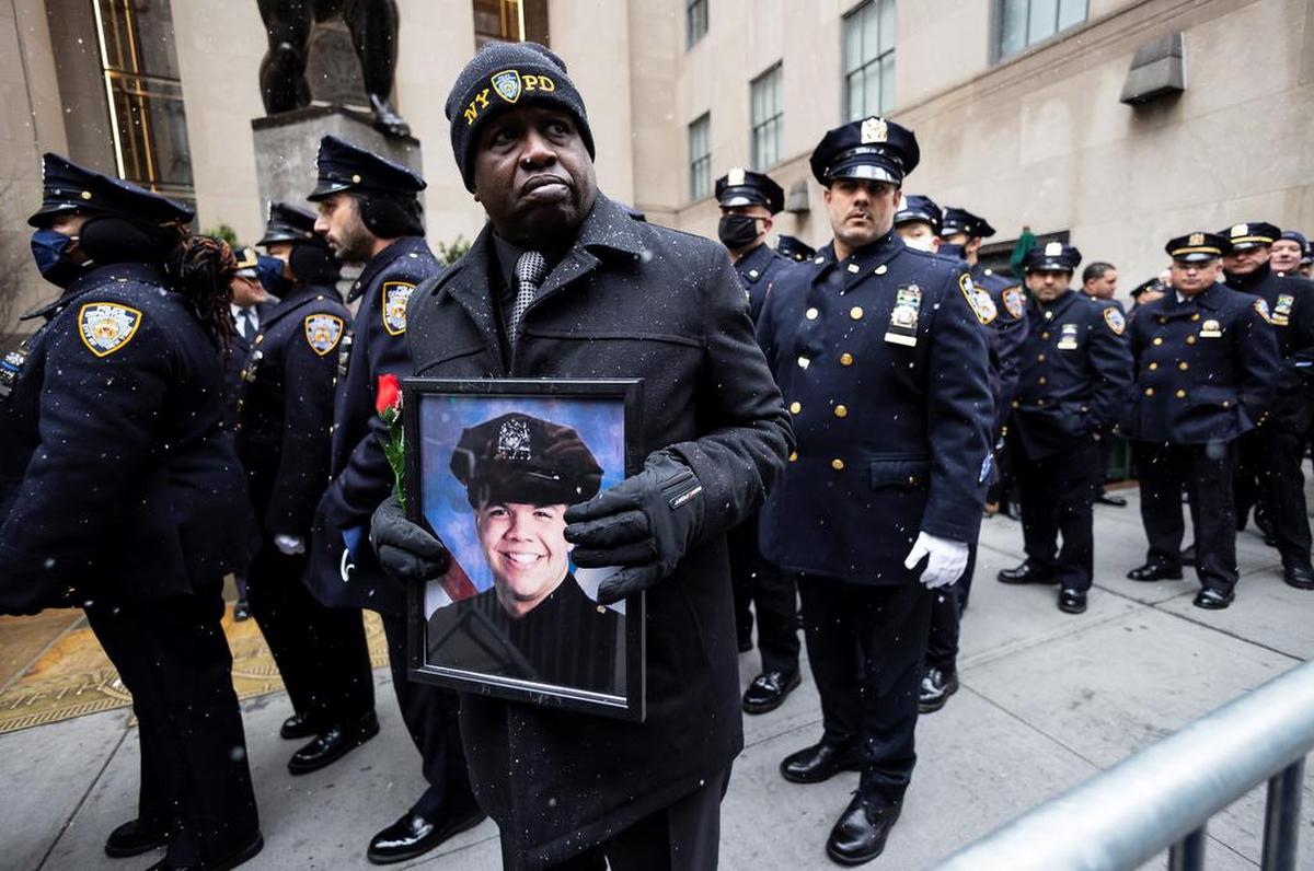 A man holds a picture of slain New York City police officer Jason Rivera outside of St. Patrick’s Cathedral during his funeral service in New York.