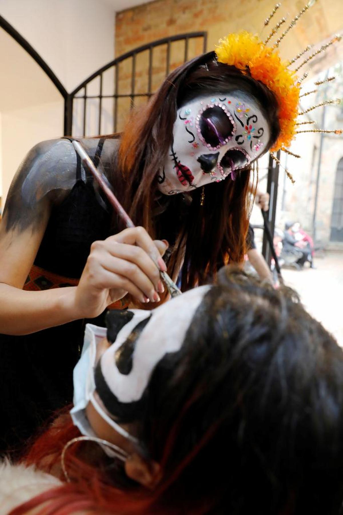 Una mujer pintada como Catrina, uno de los símbolos más característicos de la cultura mexicana, pinta a una niña durante una conmemoración del Día de Muertos en Bogotá.