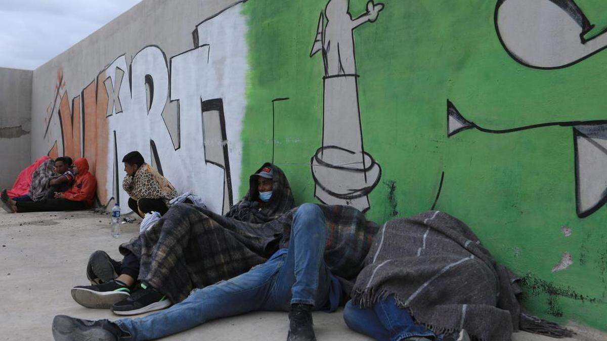 Migrantes de origen venezolano descansan en la calle cerca de la barda fronteriza entre México y Estados Unidos en Ciudad Juárez, Chihuahua.