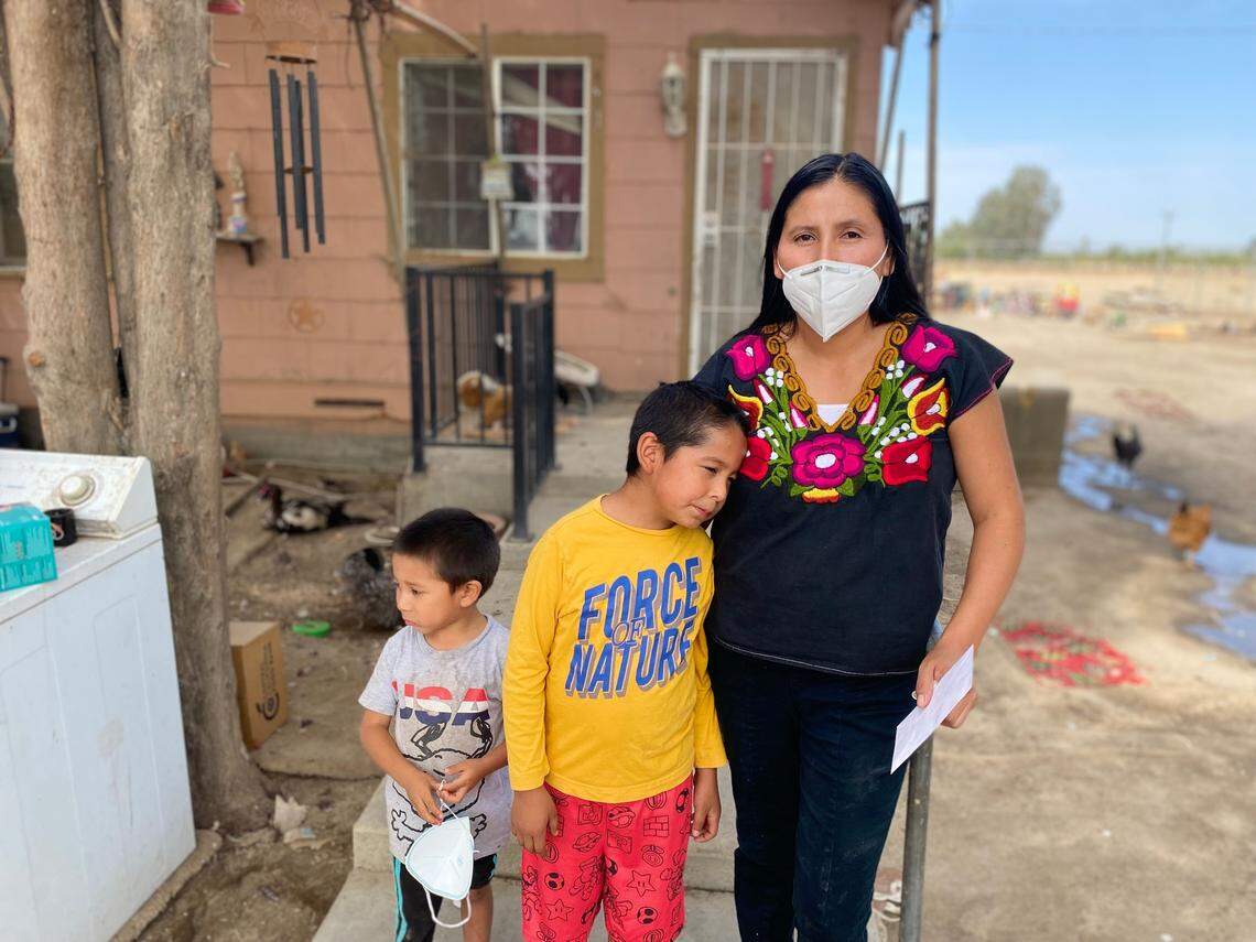 Laura García se encuentra frente a su casa en Raisin City, una pequeña comunidad no incorporada en el condado de Fresno, con sus hijos Mateo y Mattias. Su hija mayor dio positivo por COVID-19 a fines de agosto.