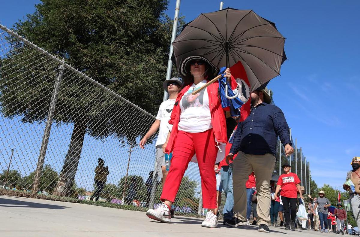 A woman uses an umbrella to protect herself from the sun during the 'March for the Governor's Signature' as it arrived at Calwa Park on Aug. 11, 2022. The 24-day march, which started Aug. 3 in Delano, ended its ninth day.
